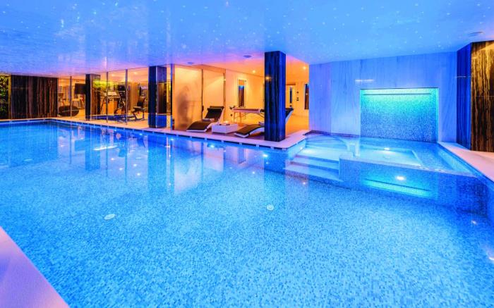 Indoor swimming pool with Jacuzzi, relaxation area and gym behind.