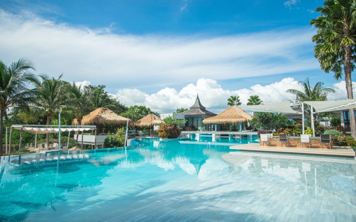 Large swimming pool surrounded by outdoor lounge areas and traditional Thai cabanas